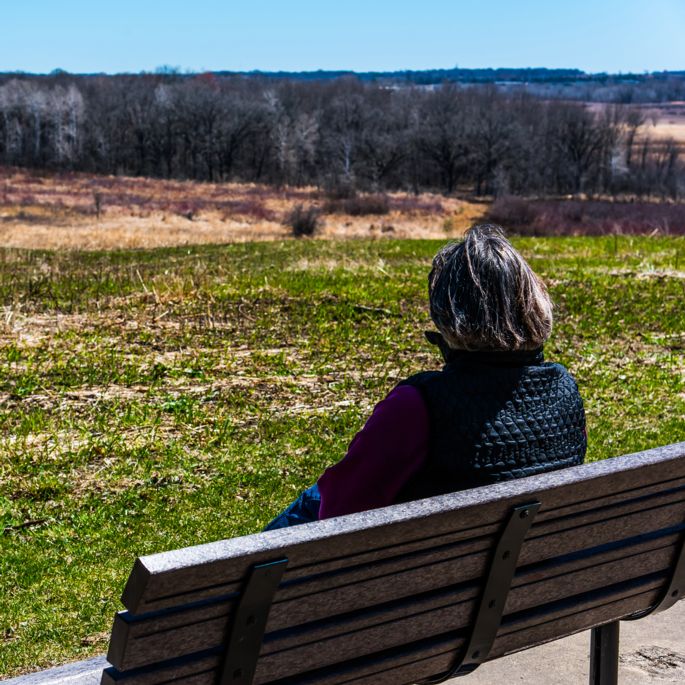 woman sitting on a bench overlooking a vast open savanna