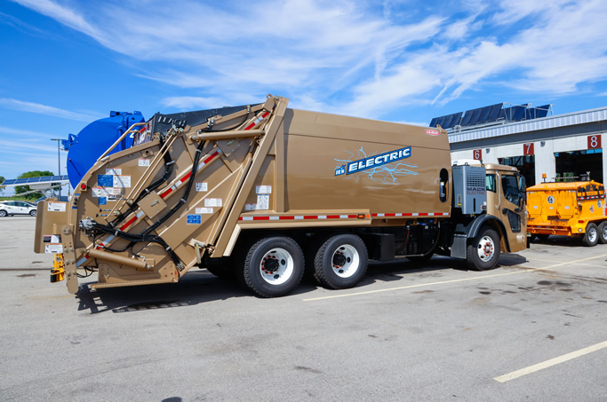 Electric rear-loading trash truck parked at the fleet garage